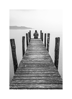 Eine einsame Frau sitzt auf einem Steg am Chiemsee